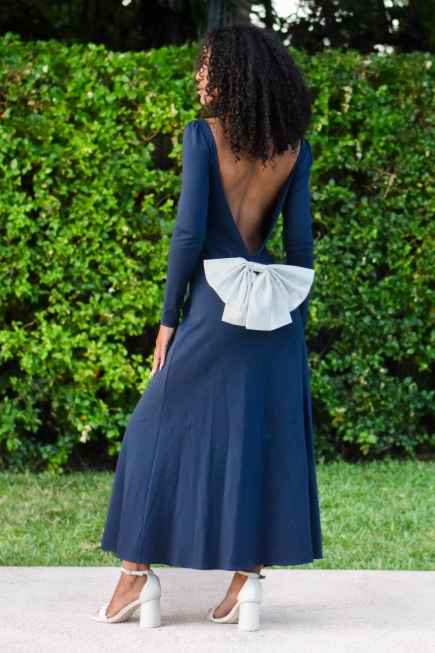 Model wearing the Pansy gown in royal navy blue with an open back and detachable bow, by the poolside.